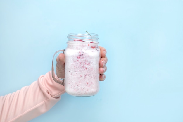 Une tasse de smoothies de baies à la main sur un fond bleu