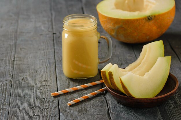 Photo tasse avec smoothies, tranches de citrouille et tubes à cocktail sur une table en bois.