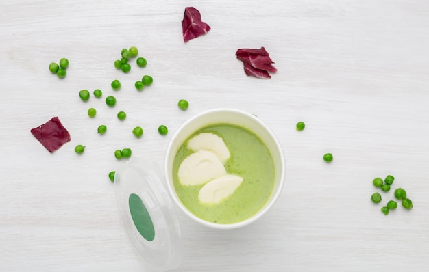 Une tasse de soupe verte avec des morceaux de légumes est sur une table blanche avec des pois verts. Concept d'alimentation saine.