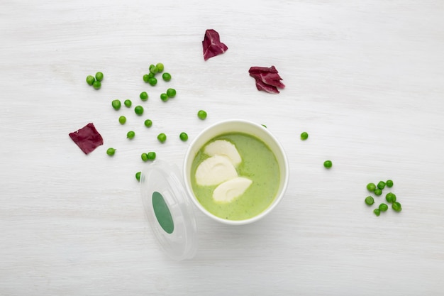 Une tasse de soupe verte avec des morceaux de légumes est sur une table blanche avec des pois verts. Concept d'alimentation saine.