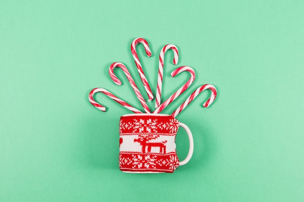 Une tasse avec des sucettes de bonbons dans un pull rouge de Noël avec un cerf sur un vert