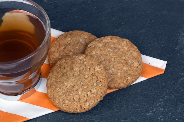 Photo tasse de thé accompagnée de biscuits à l'avoine sur une serviette à motifs sur fond sombre