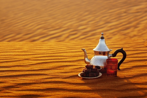Une tasse de thé arabe et des dattes dans le désert lors d'un beau coucher de soleil symbolisant le ramadan