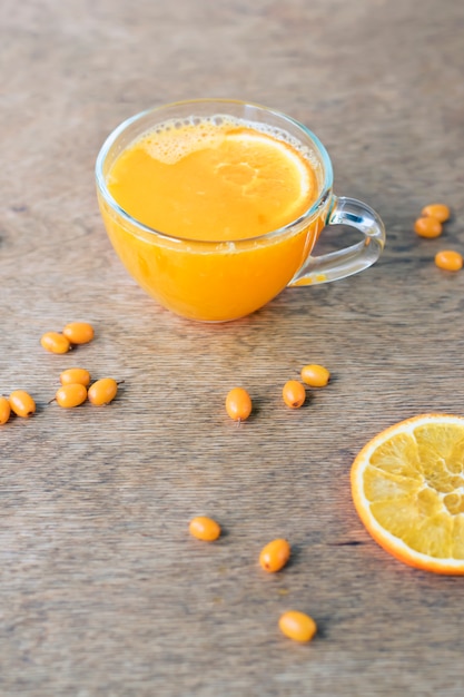 Tasse de thé d'argousier sain à l'orange sur un mur en bois.