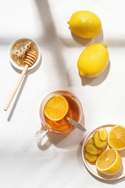 Une tasse de thé au citron et une assiette de miel avec une cuillère en bois sur une table recouverte d'une languette blanche