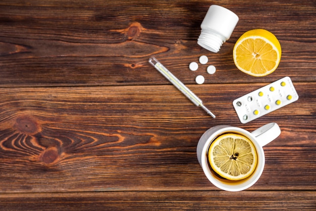 Tasse de thé au citron, citron, thermomètre et pilules sur une surface en bois. Traitement au froid. Saison de la grippe.