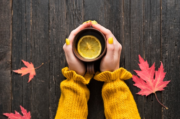 Tasse de thé au citron dans une main féminine. feuilles d'automne. Vue de dessus