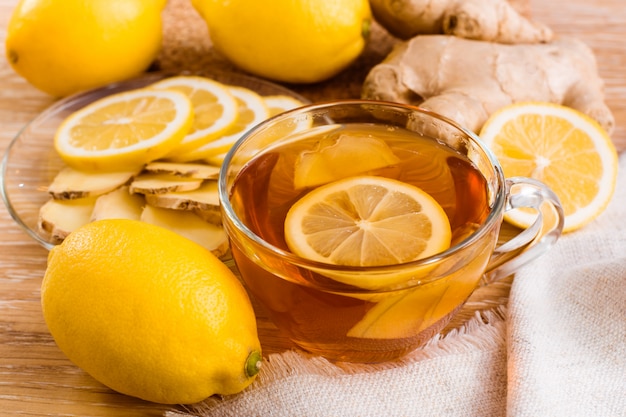 Tasse de thé au citron avec des morceaux de gingembre et de citron sur une assiette sur une table en bois