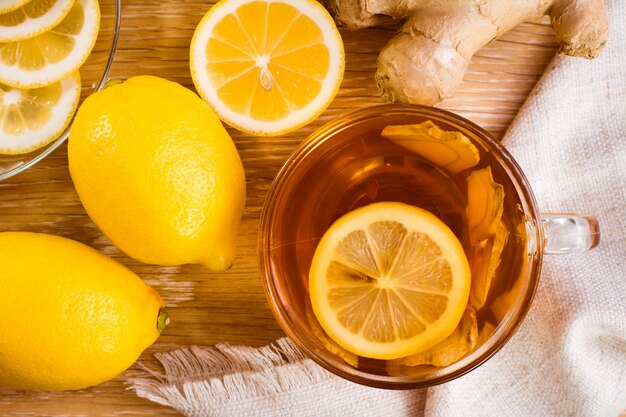 Tasse de thé au citron avec des morceaux de gingembre et de citron sur une assiette sur une table en bois