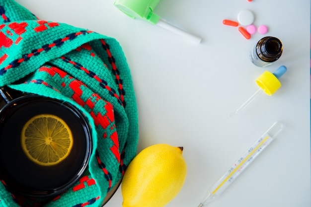 Une tasse de thé au citron se dresse sur une écharpe tricotée verte et rouge à côté d'un thermomètre à citron et...