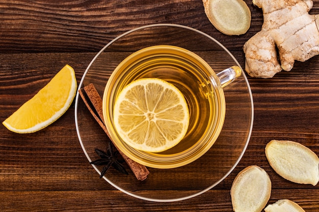 Tasse de thé au gingembre avec citron, miel et racine de gingembre sur un fond en bois, vue de dessus.