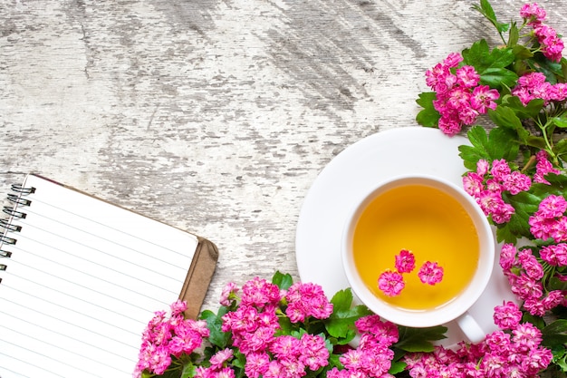 Tasse de thé aux fleurs d'été avec des branches florales roses et un cahier ligné vierge