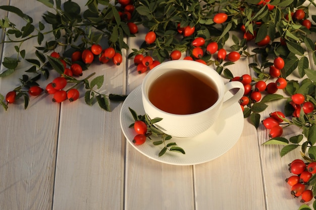 Tasse de thé avec des baies de rose sur un fond en bois blanc