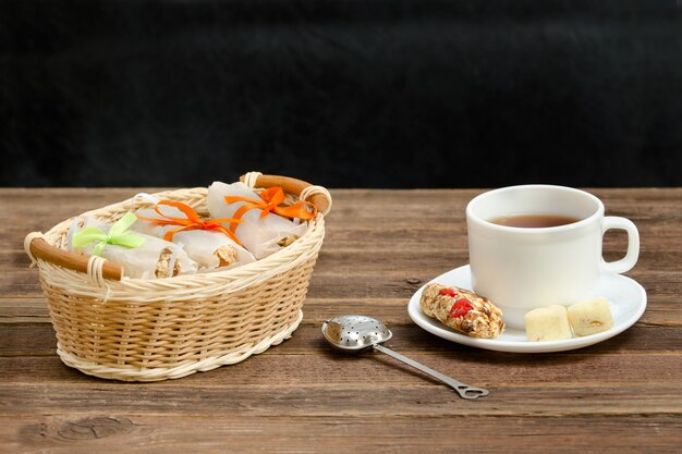 Tasse de thé, barres de muesli et passoire à thé. Panier en osier avec des barres. Bois brun