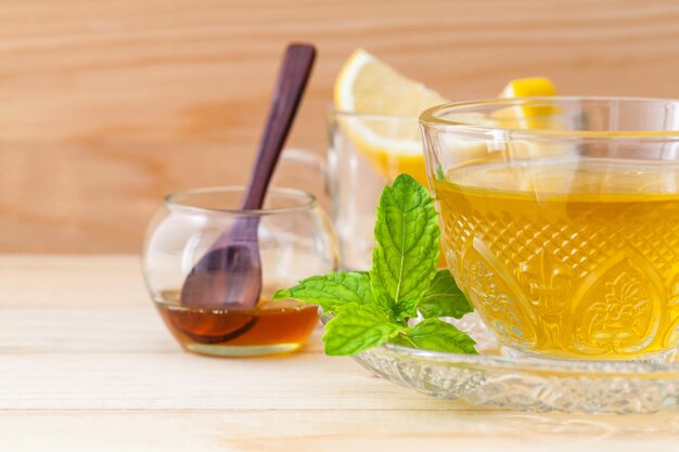 Une tasse de thé à base de plantes avec du miel de menthe verte fraîche et du citron sur fond de bois