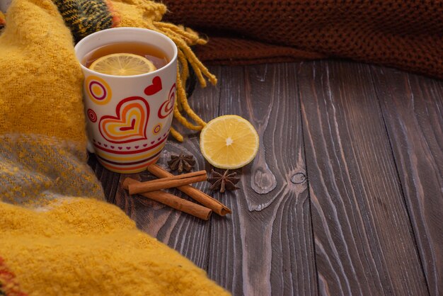 Une tasse de thé avec des bâtons de citron et de cannelle sur une table en bois humeur d'automne snood tricoté chaud