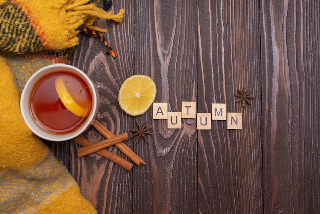 Une tasse de thé avec des bâtons de citron et de cannelle sur une table en bois humeur d'automne snood tricoté chaud