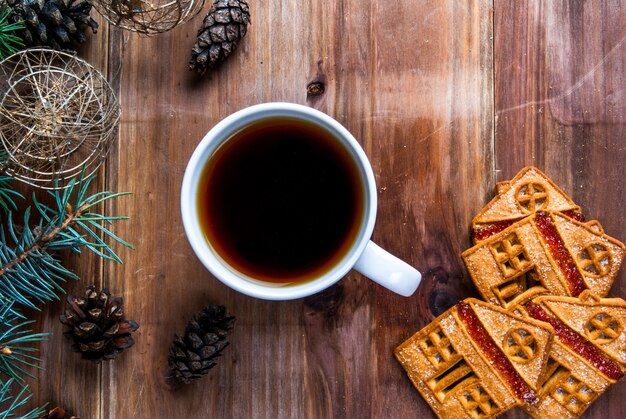 tasse de thé et biscuits sur une table en bois. Près de la branche d'arbre de Noël, des pommes de pin et des boules de Noël.