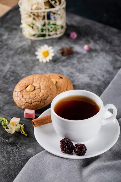 Une tasse de thé blanc avec des baies, de la cannelle et des biscuits sur une nappe