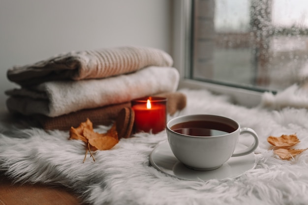 Une tasse de thé et une bougie allumée sur le rebord de la fenêtre. Photo d'automne confortable.