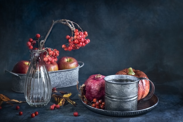 Une tasse de thé une branche de sorbier dans un vase et des fruits sur un fond grunge vintage automne nature morte...