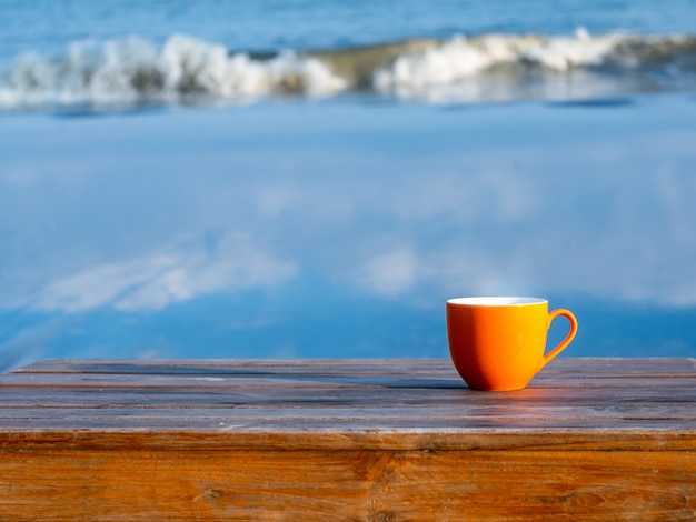 Tasse de thé ou de café sur une table en bois sur la plage, vue mer