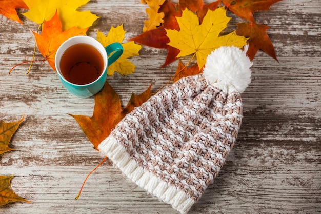 Une tasse de thé, chapeau d'automne, feuilles jaunes et rouges. sur surface en bois