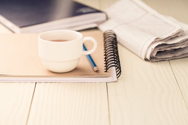 Tasse de thé chaud sur un cahier sur une table en bois blanche.