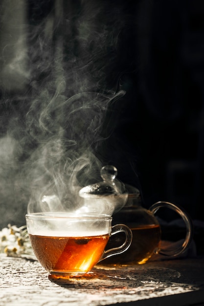 Tasse de thé chaud avec théière en verre sur fond sombre