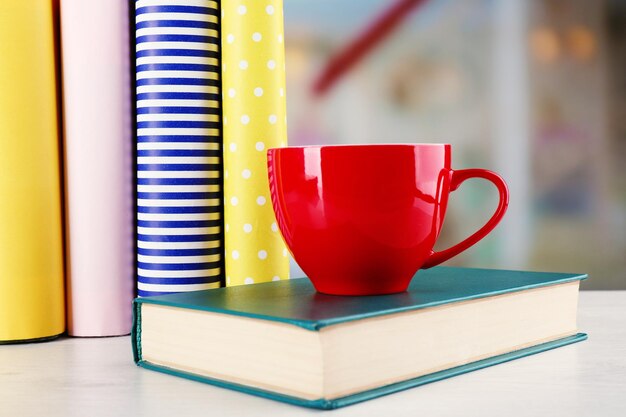 Tasse de thé de couleur avec des livres sur la table sur fond flou clair