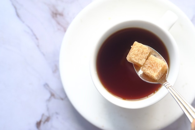 Tasse de thé et cube de sucre brun sur table.