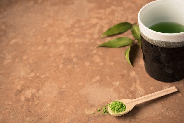 Tasse de thé avec du thé vert en poudre dans une cuillère en bois sur la table.