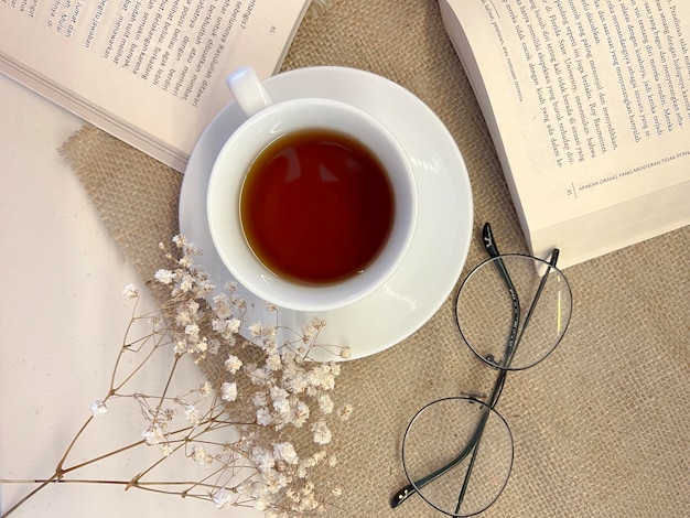 Une tasse de thé est placée sur la table à côté de lunettes de livre ouvertes et de fleurs séchées