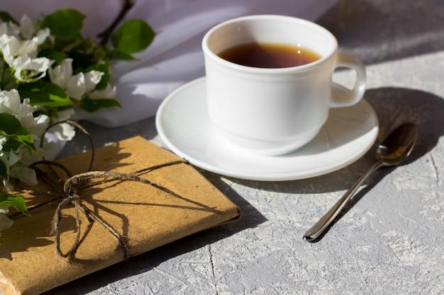 Tasse de thé avec une fleur de printemps fraîche. Petit déjeuner à l'extérieur par une journée ensoleillée. Jolie boîte cadeau enveloppée de papier kraft brun simple et décorée de jute. Concept de préparation pour les vacances