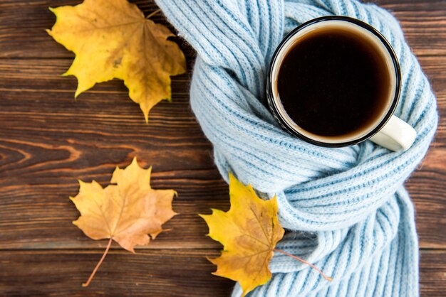 Tasse à thé avec foulard bleu et feuilles d'automne sur fond de bois. Saison grippale en automne, maladie.