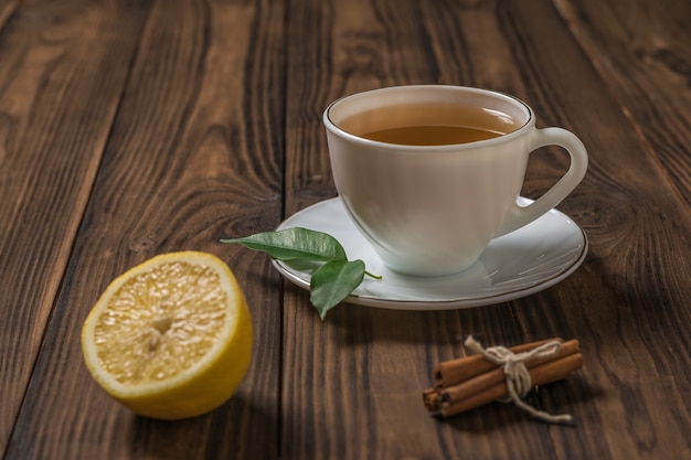 Une tasse de thé frais avec un demi-citron et des bâtons de cannelle sur une table en bois. Une boisson vivifiante utile pour la santé.