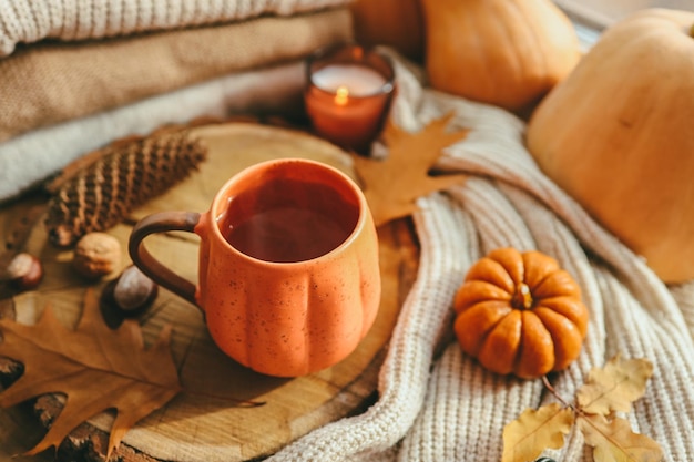 Une tasse de thé fumant chaud et une bougie en forme de citrouille sur le rebord de la fenêtre