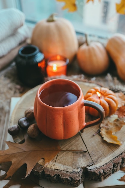 Une tasse de thé fumant chaud et une bougie en forme de citrouille sur le rebord de la fenêtre