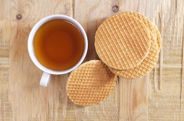 Une tasse de thé et des gaufrettes rondes au caramel sont situées sur une vieille surface en bois, vue de dessus