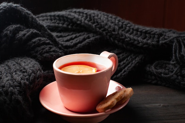 Une tasse de thé à la grenade rose et un foulard tricoté sur fond de bois noir
