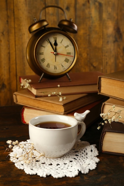 Tasse de thé avec des livres et horloge sur fond de bois