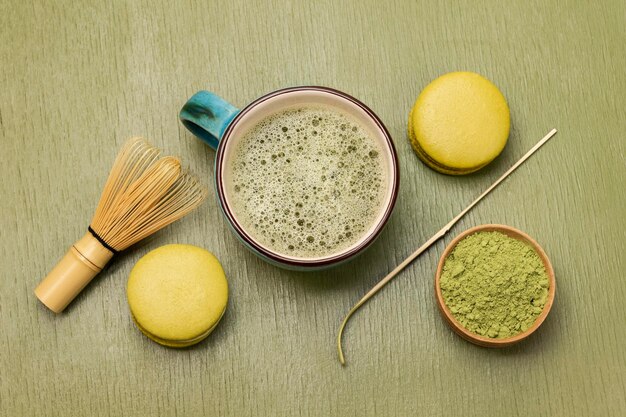 Une tasse de thé Matcha et de poudre de thé Matcha dans un bol Fouet et cuillère en bambou Gâteau Macaron Fond vert