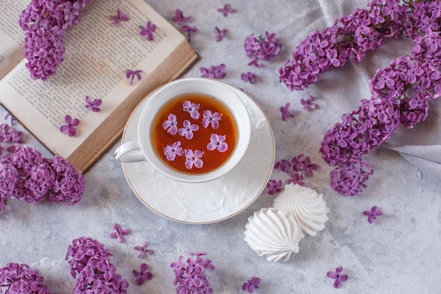 Une tasse de thé, meringue, branches de lilas en fleurs et un vieux livre