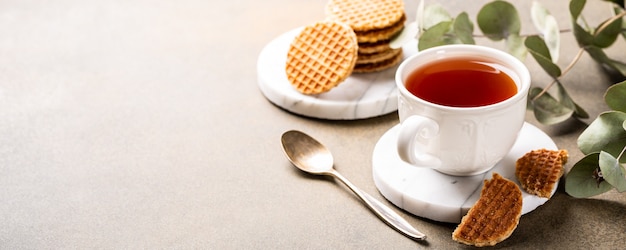 Tasse de thé avec mini stroopwafel, biscuits siropwaffles et brindilles d'eucalyptus sur une surface claire avec espace de copie. Bannière