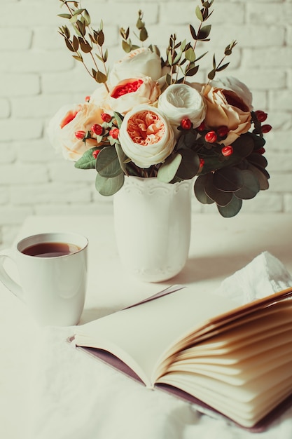 Une tasse de thé noir, un cahier et de belles fleurs sur la table. Inspiration du matin pour la planification de la journée