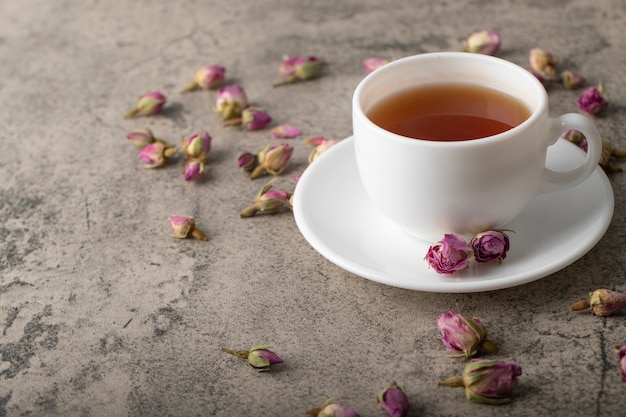 Tasse de thé noir chaud avec des roses séchées sur la surface de la pierre.