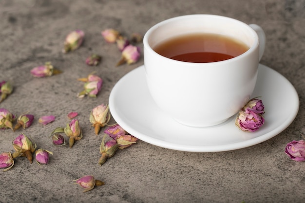 Tasse de thé noir chaud avec des roses séchées sur la surface de la pierre.