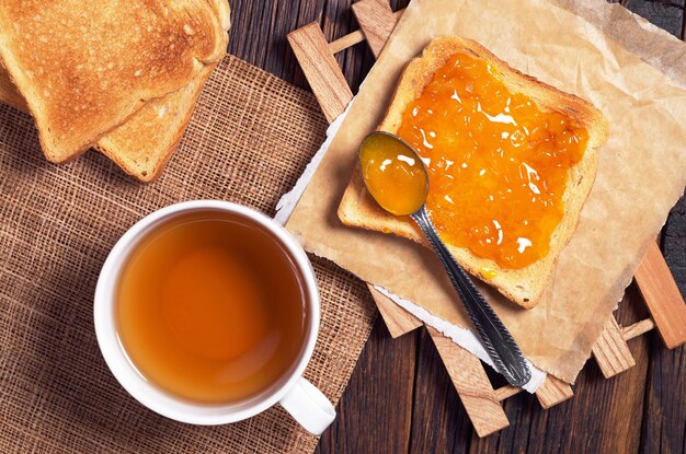 Tasse de thé noir et pain grillé avec de la confiture d'abricot sur la vue de dessus de table en bois