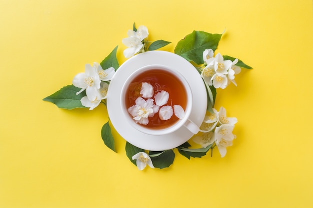 Tasse de thé avec des pétales de fleurs de jasmin sur un jaune vif