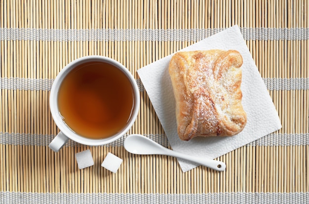 Tasse de thé et petit pain sucré de pâte feuilletée avec de la confiture sur une serviette en bambou